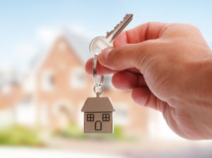 Holding house keys on house shaped keychain in front of a new home